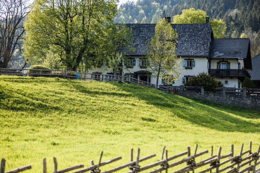 Auf dem Bild ist ein Haus zu sehen, welches auf hinter eine grünen Wiese steht.